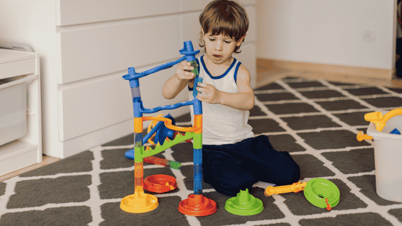 A 3-year-old preschooler engaged in deep pretend play with a wooden play kitchen and toy food, developing social and emotional skills.