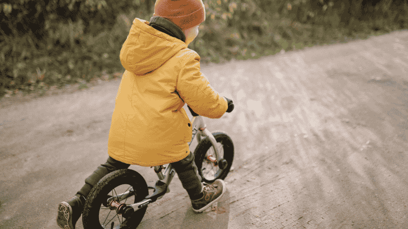 A 3-year-old child confidently riding a 3-wheeled Micro Mini Deluxe scooter on a paved path, practicing balance and coordination.