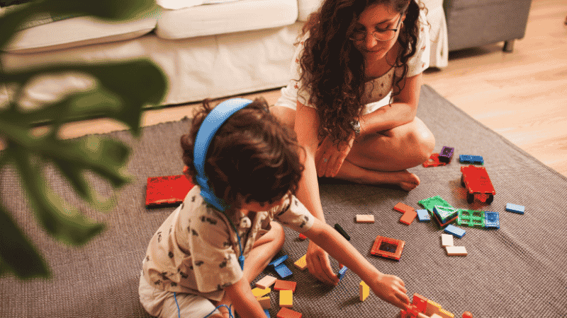 Two 3-year-old kids collaborating and sharing building blocks on a play mat, demonstrating early cooperative play milestones.