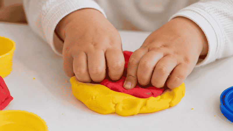 Close-up of a 2-year-old toddler's hands squeezing and pressing colorful play dough, building fine motor skills
