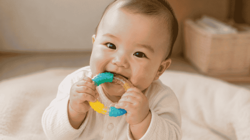 A 5-month-old baby happily chewing on a colorful food-grade silicone teether ring, supporting oral sensory development