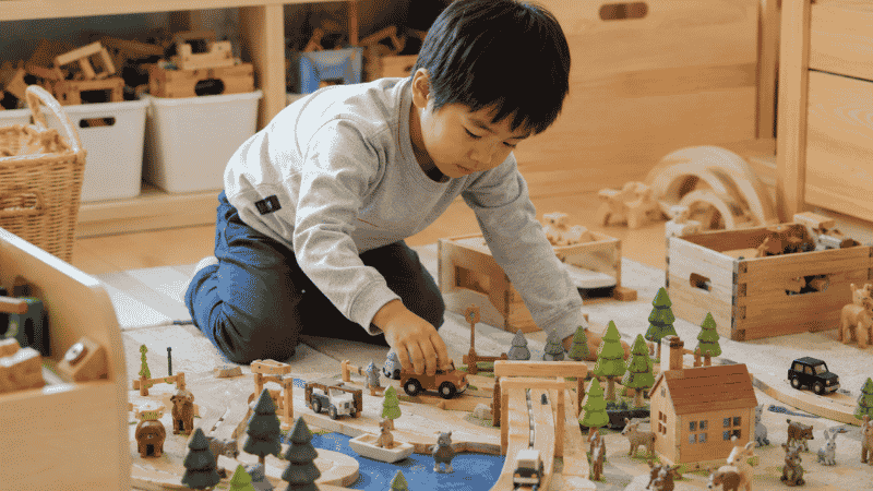 A 5-year-old child arranging small wooden figures and vehicles in an imaginative small-world play scene on the floor