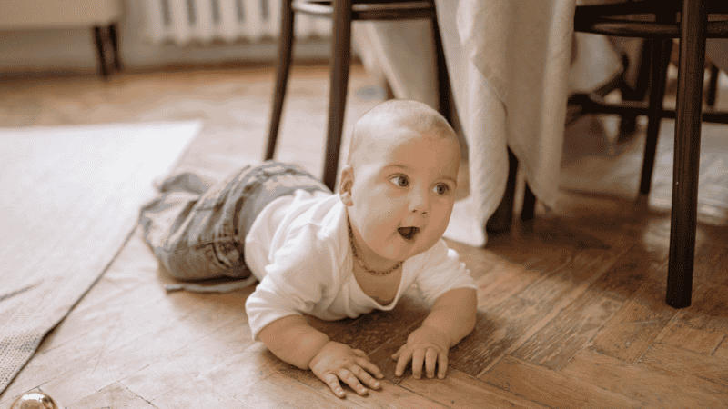 A one-year-old toddler happily pushing a sturdy wooden walker wagon across a hardwood living room floor, practicing their first steps.