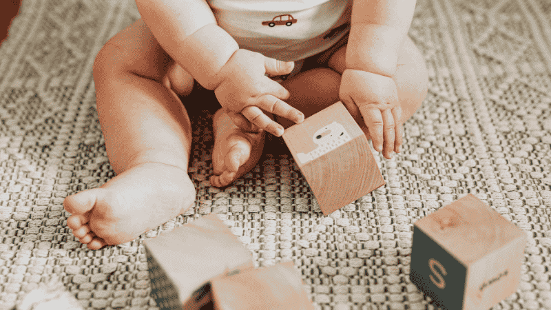 A close-up shot of a toddler's hands carefully stacking colorful wooden blocks on a low play table, demonstrating fine motor skill development.