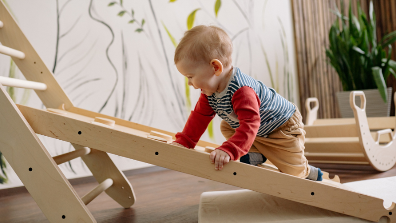 A toddler climbing a Montessori Pikler triangle, one of the best active play toys for toddlers to burn energy indoors.