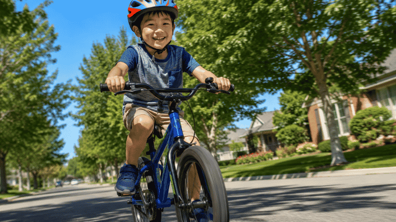 A confident 6-year-old child riding a two-wheel bike without training wheels on a sunny street wearing a colorful helmet and smiling