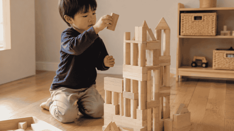 A 4-year-old child carefully building a tall structure with wooden unit blocks, developing early engineering and spatial reasoning skills