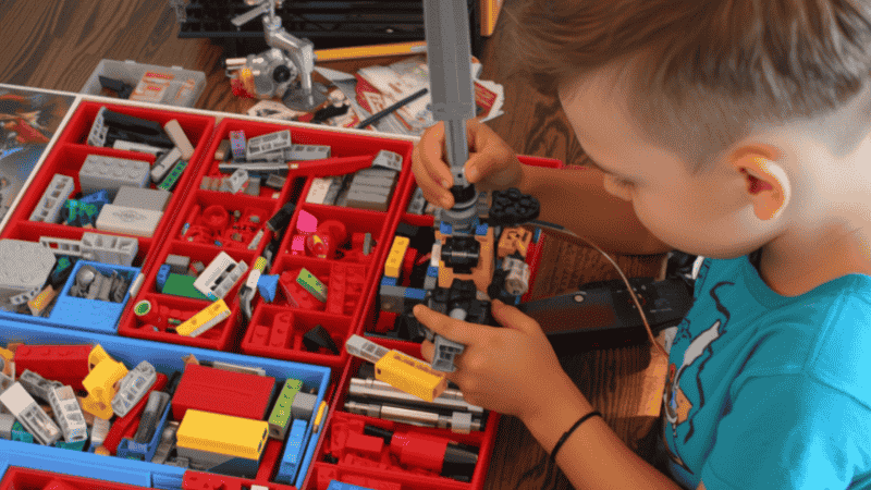 An 11-year-old child sitting at a desk, deeply focused on assembling a complex LEGO Ideas set with hundreds of pieces organized in sorting trays.