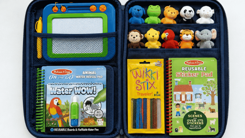 Overhead flat lay of a neatly organized travel toy pouch showing a magnetic drawing board, Water Wow book, finger puppets, Wikki Stix and sticker book arranged on a white surface